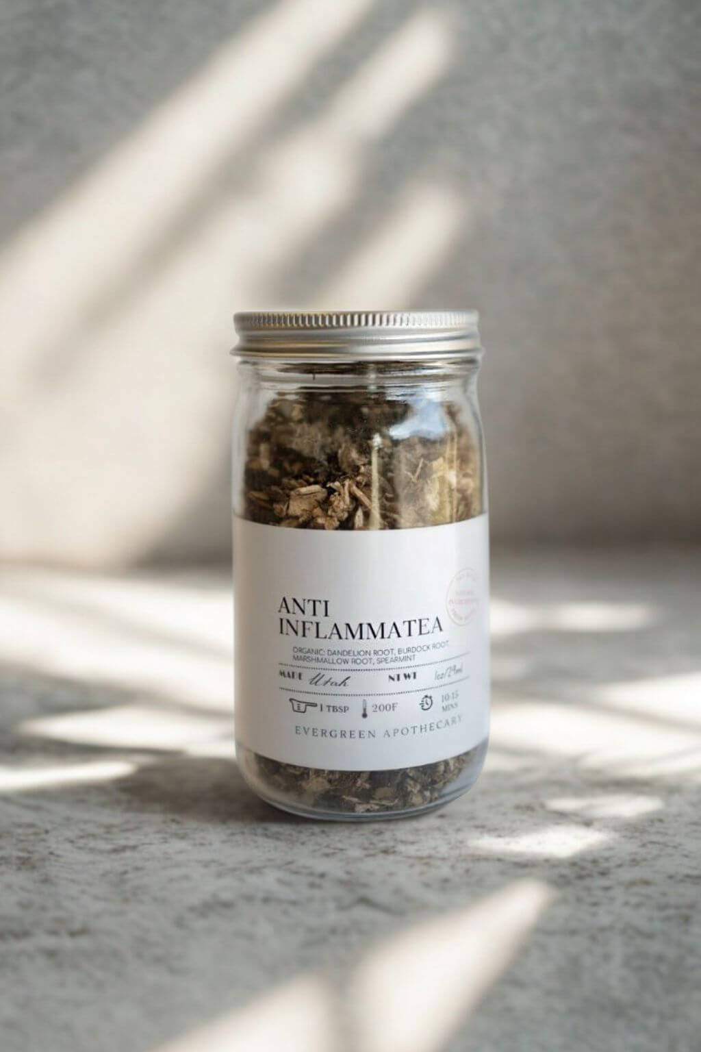 Glass jar of Evergreen Apothecary Anti-Inflammatea loose-leaf tea on stone surface with sunlight shadows
