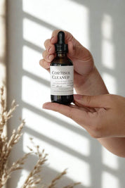 Hand holding amber glass dropper bottle of Cortisol Cleanup Tincture by Evergreen Apothecary
