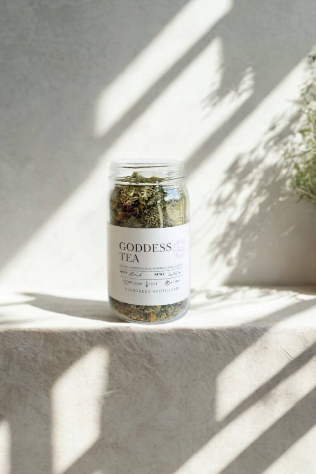 Goddess Tea in glass jar with sunlight and soft shadows on stone surface
