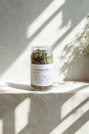 Goddess Tea in glass jar with sunlight and soft shadows on stone surface