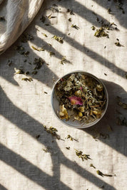 Loose leaf Goddess Tea blend with chamomile flowers and rose petals on linen cloth
