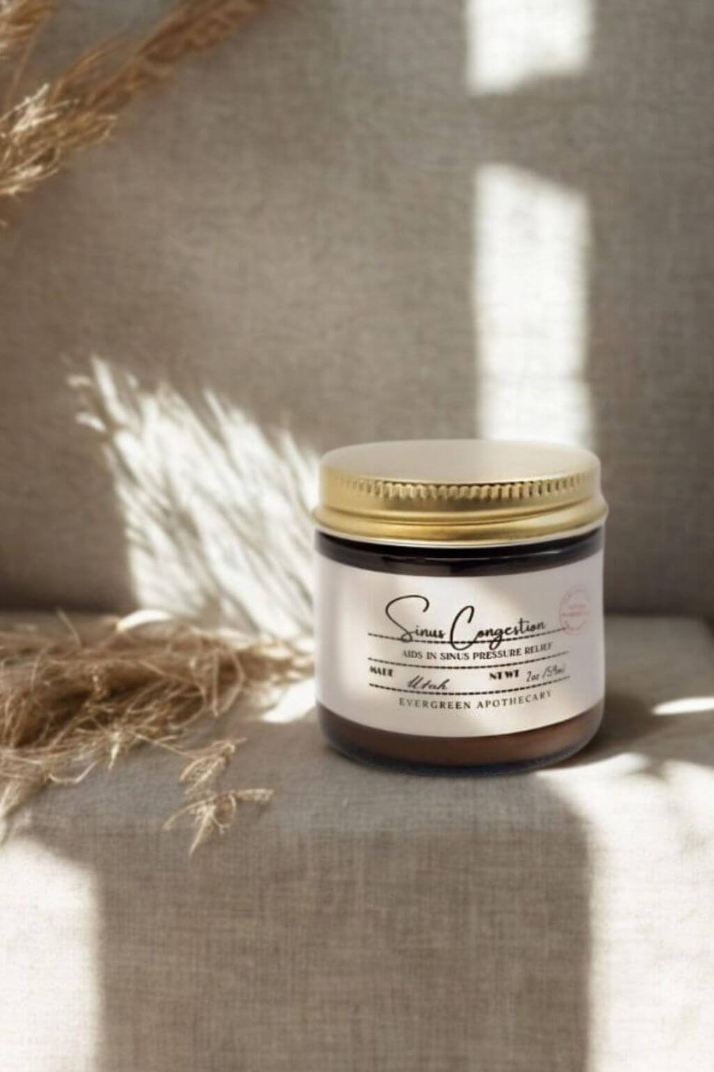 Amber glass jar of Evergreen Apothecary Sinus Congestion Salve on linen surface with soft light