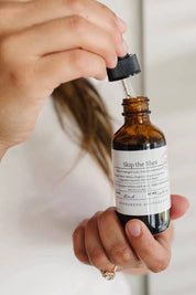 Hand holding open Skip the Shot tincture bottle with dropper above amber glass bottle