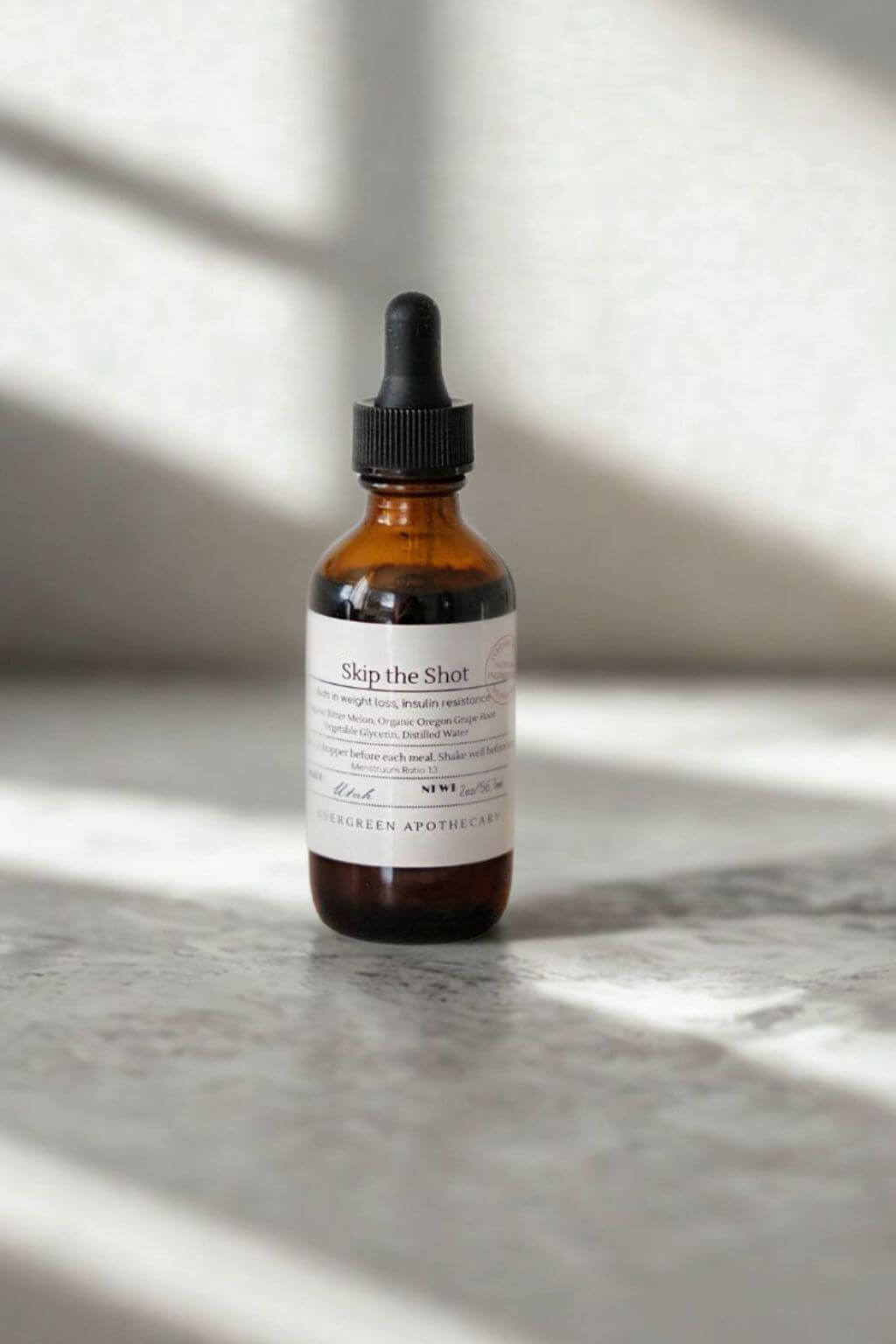 Amber glass dropper bottle of Skip the Shot tincture by Evergreen Apothecary on stone surface with soft sunlight
