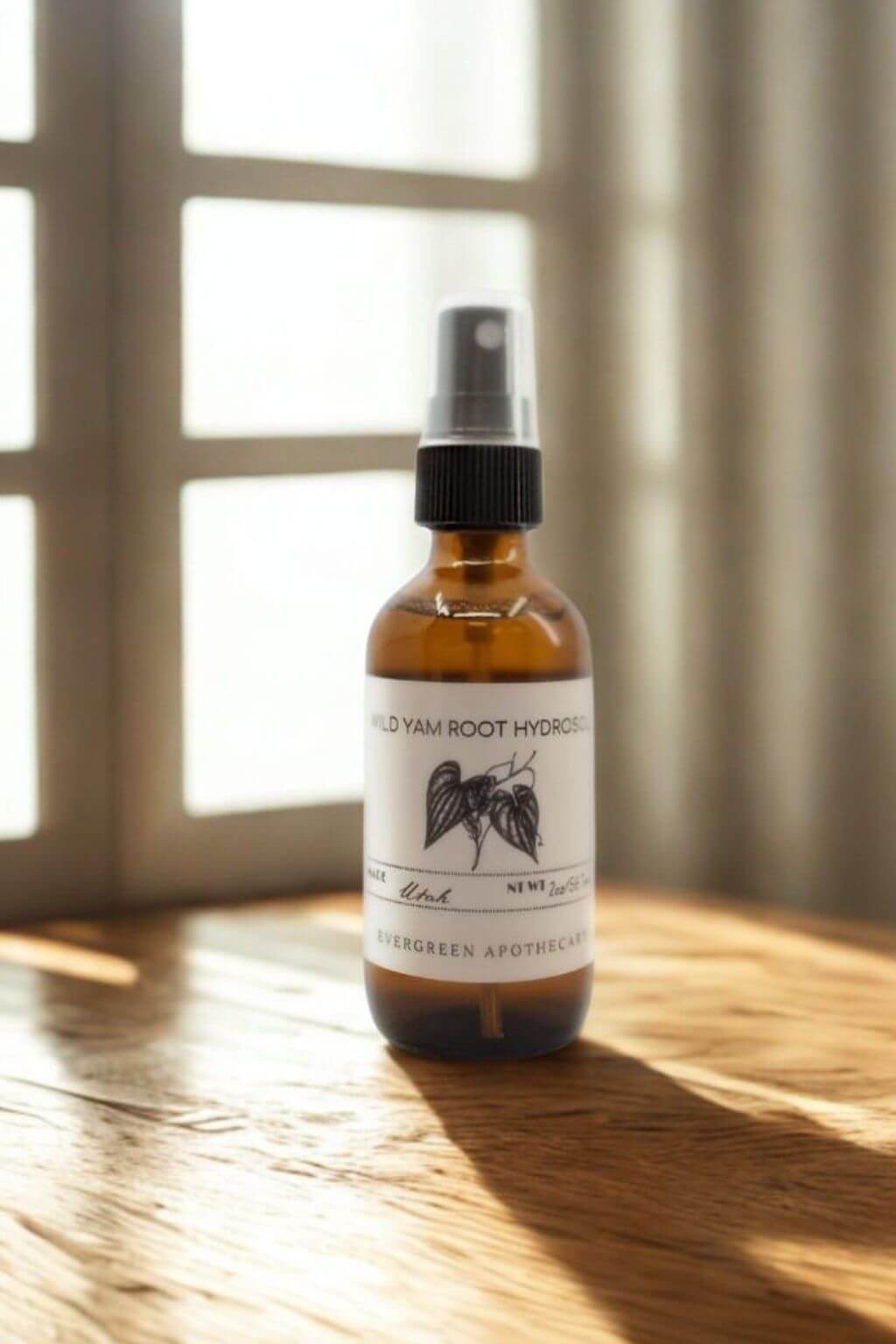 Amber glass bottle of Evergreen Apothecary Wild Yam Root Hydrosol on wood table with sunlight and window background
