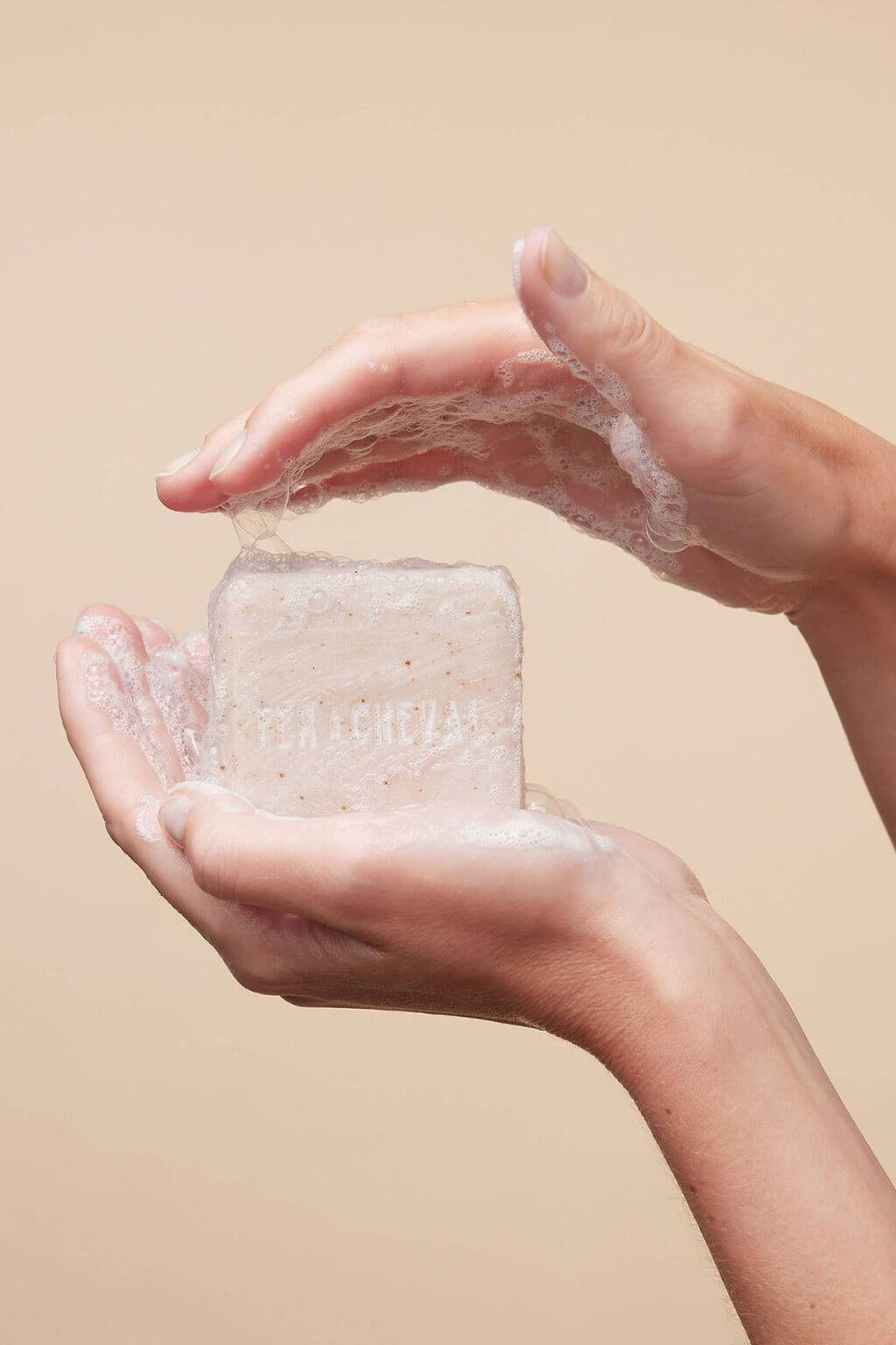 Hands holding Fer à Cheval Gentle Cleansing Soap with lathered foam, close-up on natural texture.