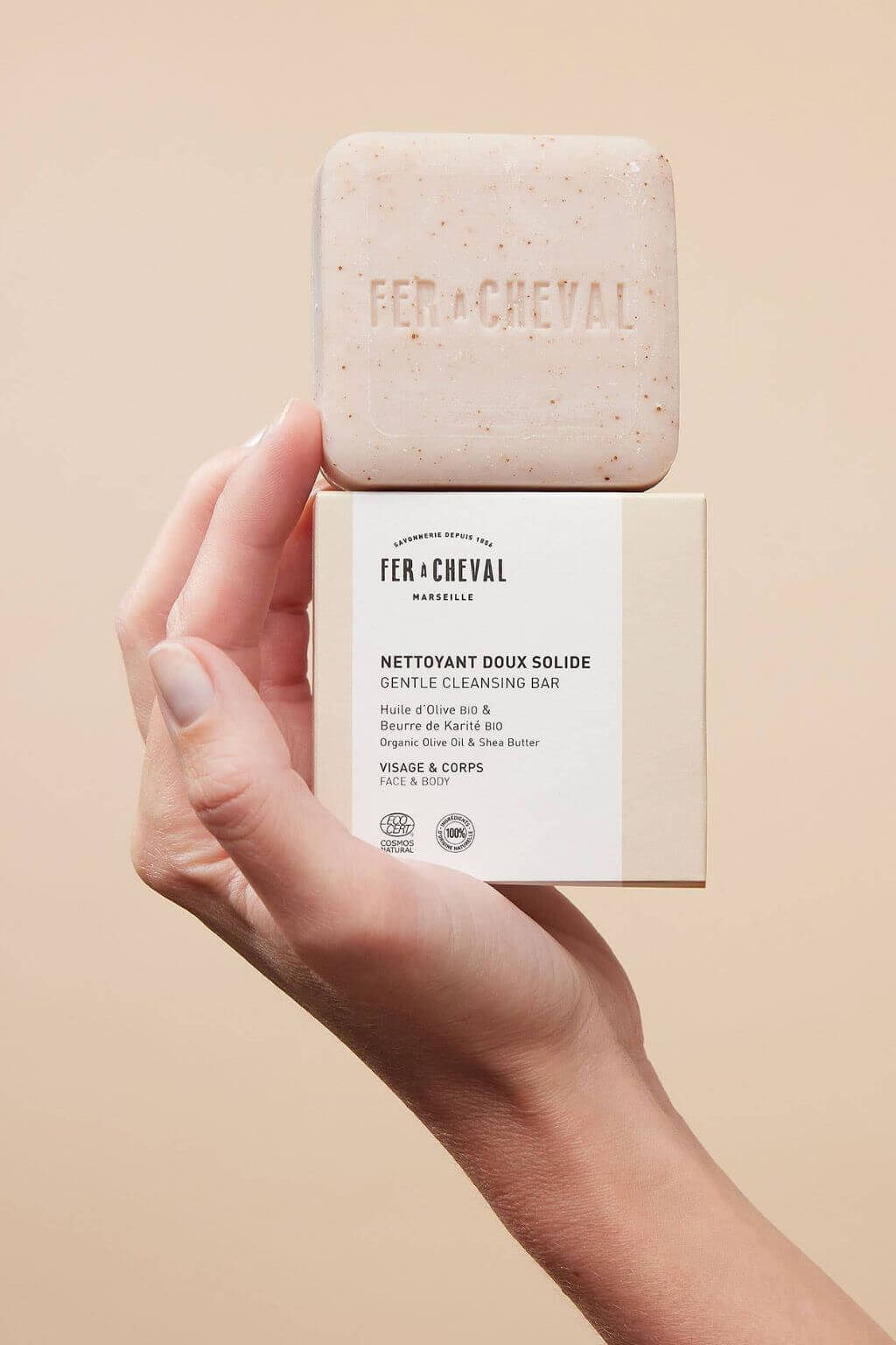 Hand holding Fer à Cheval Gentle Cleansing Soap and its box together, showcasing embossed branding.