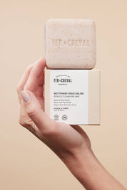Hand holding Fer à Cheval Gentle Cleansing Soap and its box together, showcasing embossed branding.