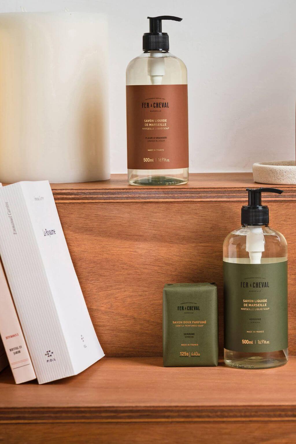 Fer à Cheval Marseille Liquid Soap Orange Blossom bottle and Verbena bottle on wooden shelf with soaps.
