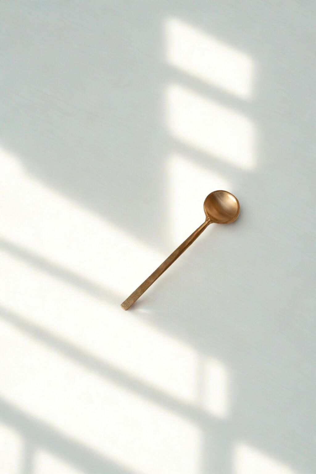 Single Wabi Petite Brass Coffee Spoon resting in soft light and shadow