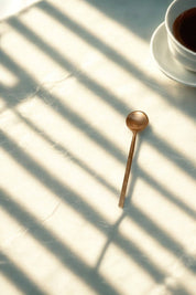 Wabi Petite Brass Coffee Spoon beside a ceramic cup in natural light