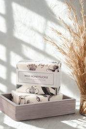 Two Wild Honeysuckle bath bars resting in a wooden soap tray, sunlight streaming in.