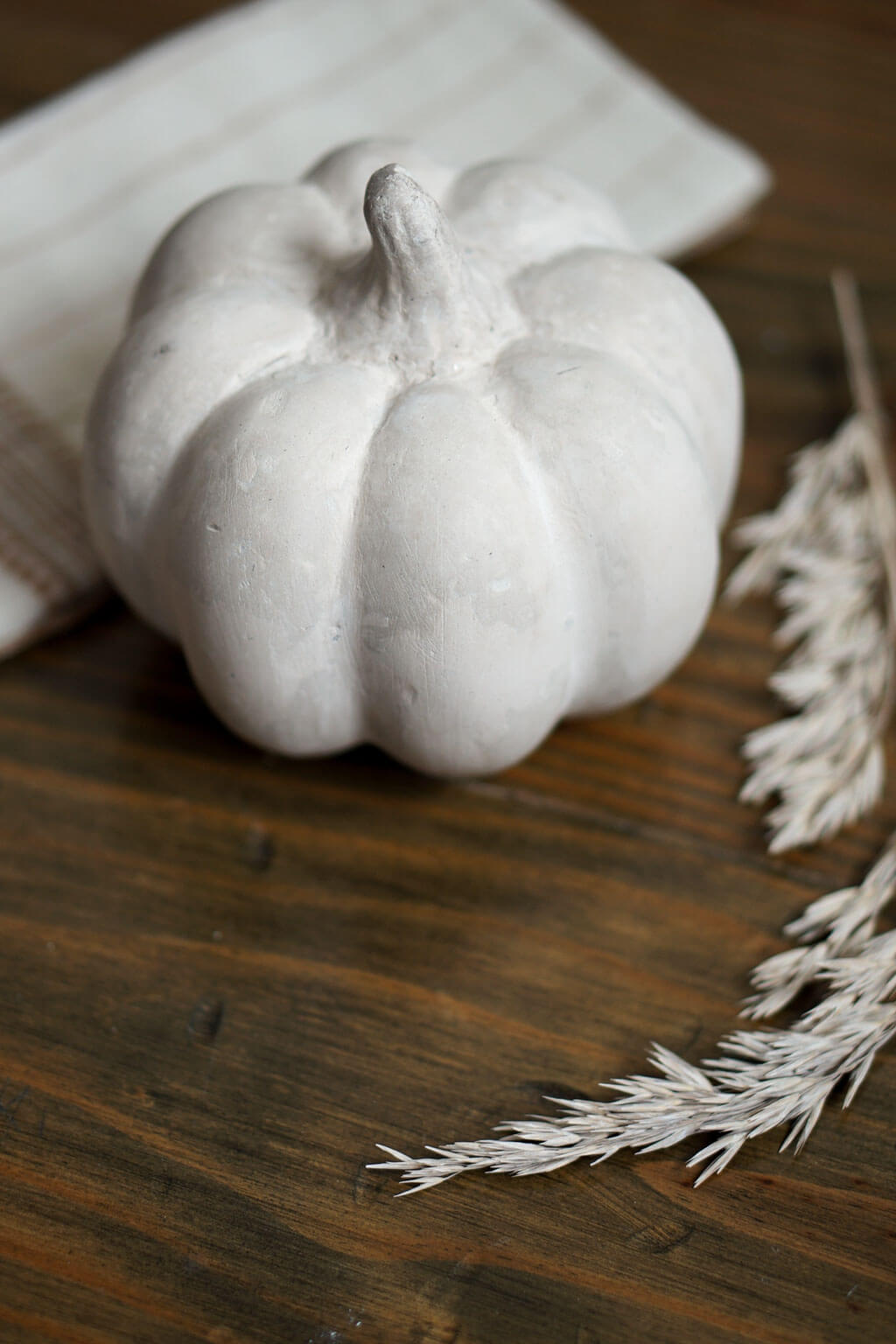 Decorative papier mache pumpkin clay-like texture on a wooden surface with dried leaves