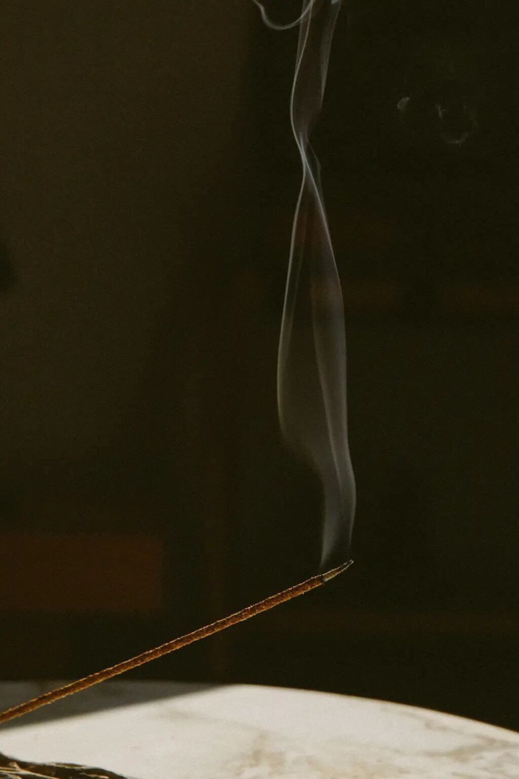 Thin stream of smoke rising from a stick of incense against a dark background