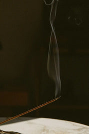 Thin stream of smoke rising from a stick of incense against a dark background