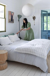 Woman in a green dress in a bright, airy bedroom, spraying her pillow and bedding with Koala Eco's Natural Pillow and Linen Spray