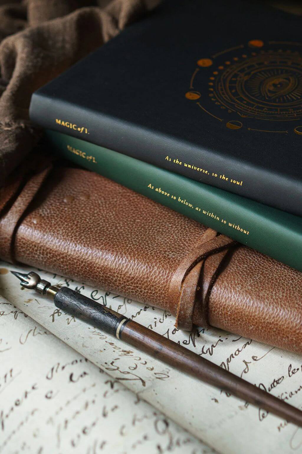Magic of I 2026 Astrological Planners in Black and Green stacked upon an old leather journal