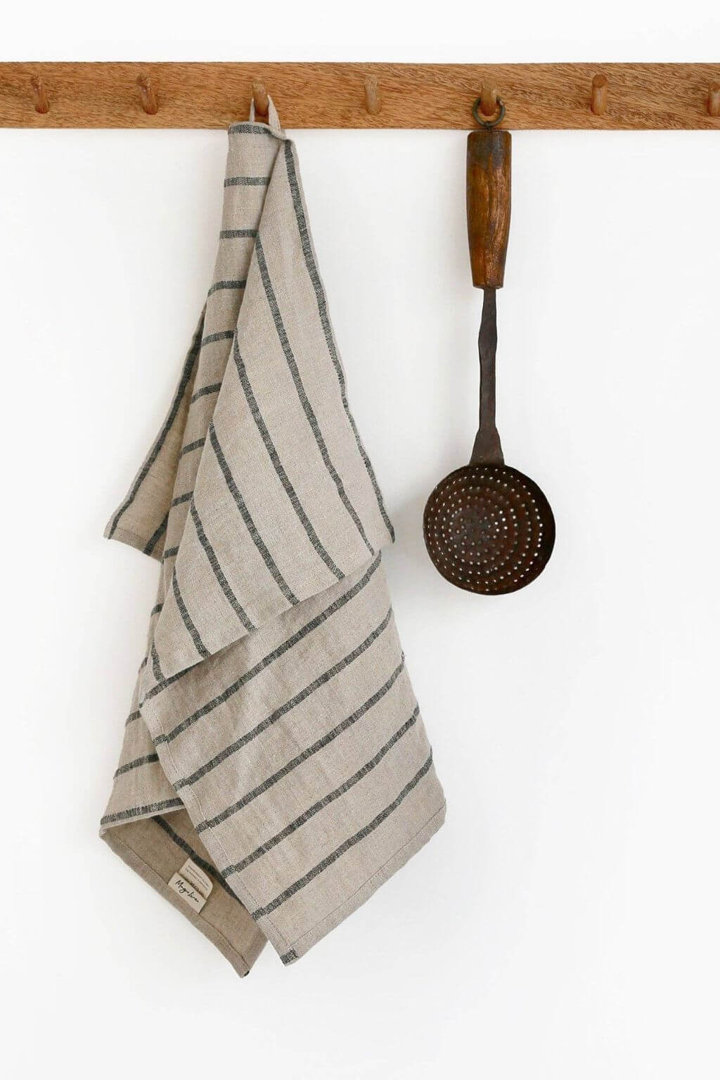 Striped linen towel hanging on a wooden rack with a spatula next to it against a white background