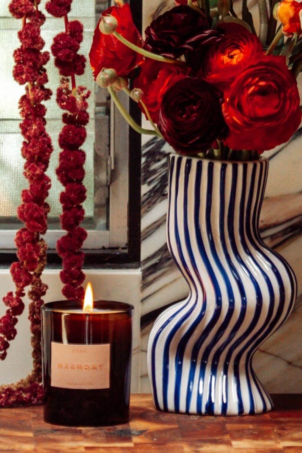 Marmont candle burning beside striped ceramic vase and florals