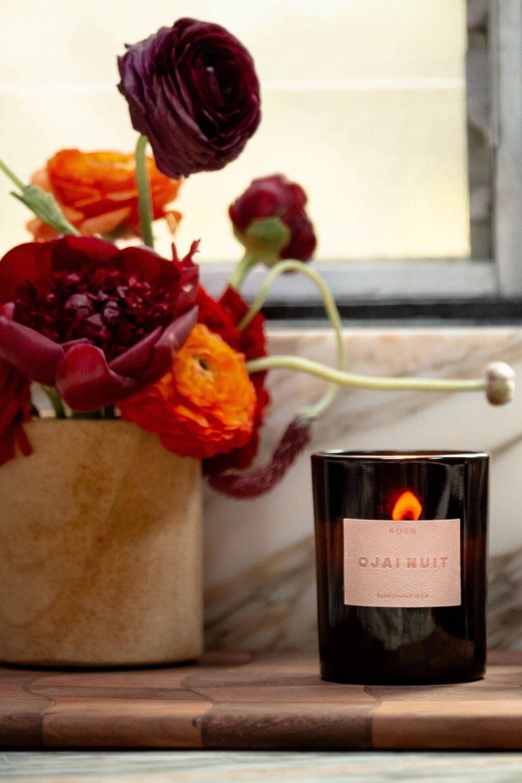 Ojai Nuit candle glowing beside bold florals