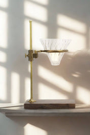 The Clerk brass and walnut pour-over coffee stand in sunlight with glass Hario V60 dripper.