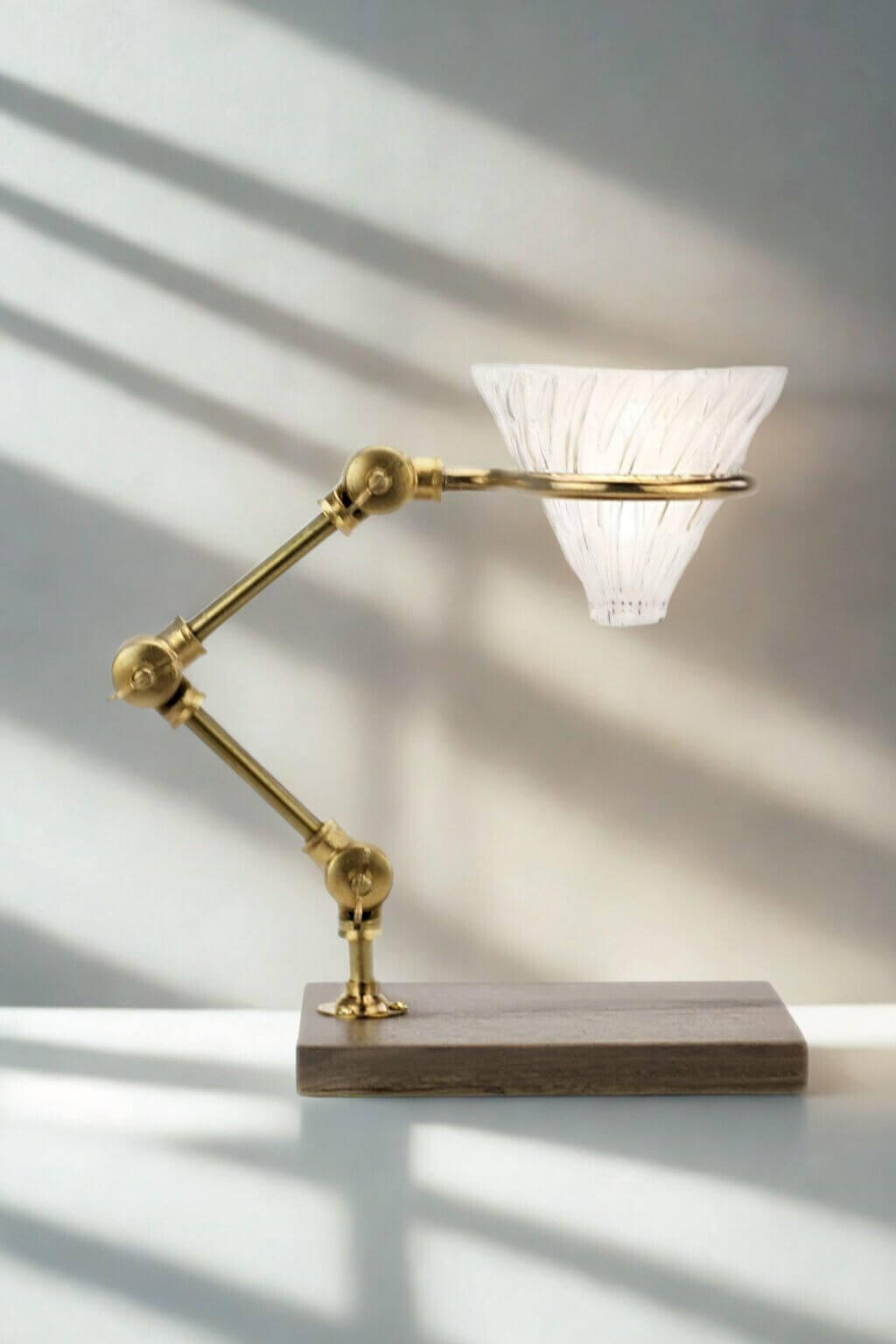 The Curator brass pour-over coffee stand with glass dripper on walnut base.