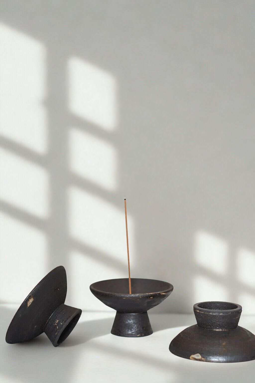 Three handcrafted incense holders in raw black stoneware with minimalist forms and natural imperfections.