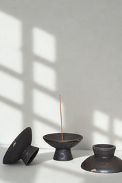 Three handcrafted incense holders in raw black stoneware with minimalist forms and natural imperfections.
