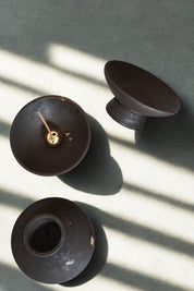 Overhead view of three black stoneware incense holders showing their wheel-thrown texture and brass dome insert.